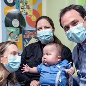Masked adults surround young child in an exam room.