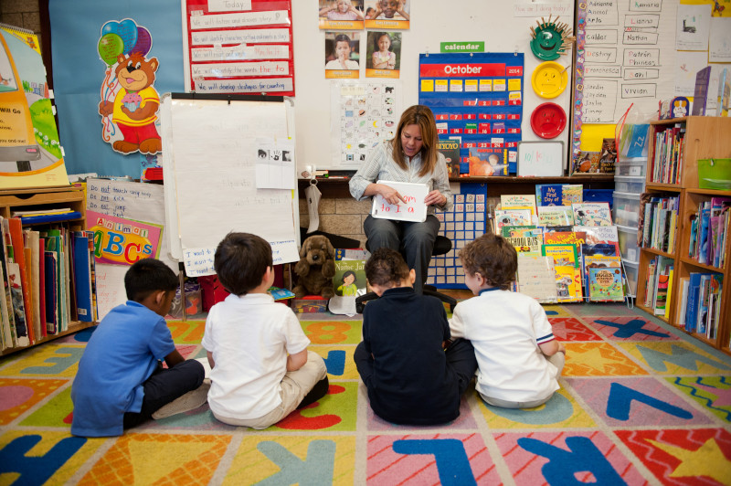 Woman sitting in chair reads to students who are sitting on the floor