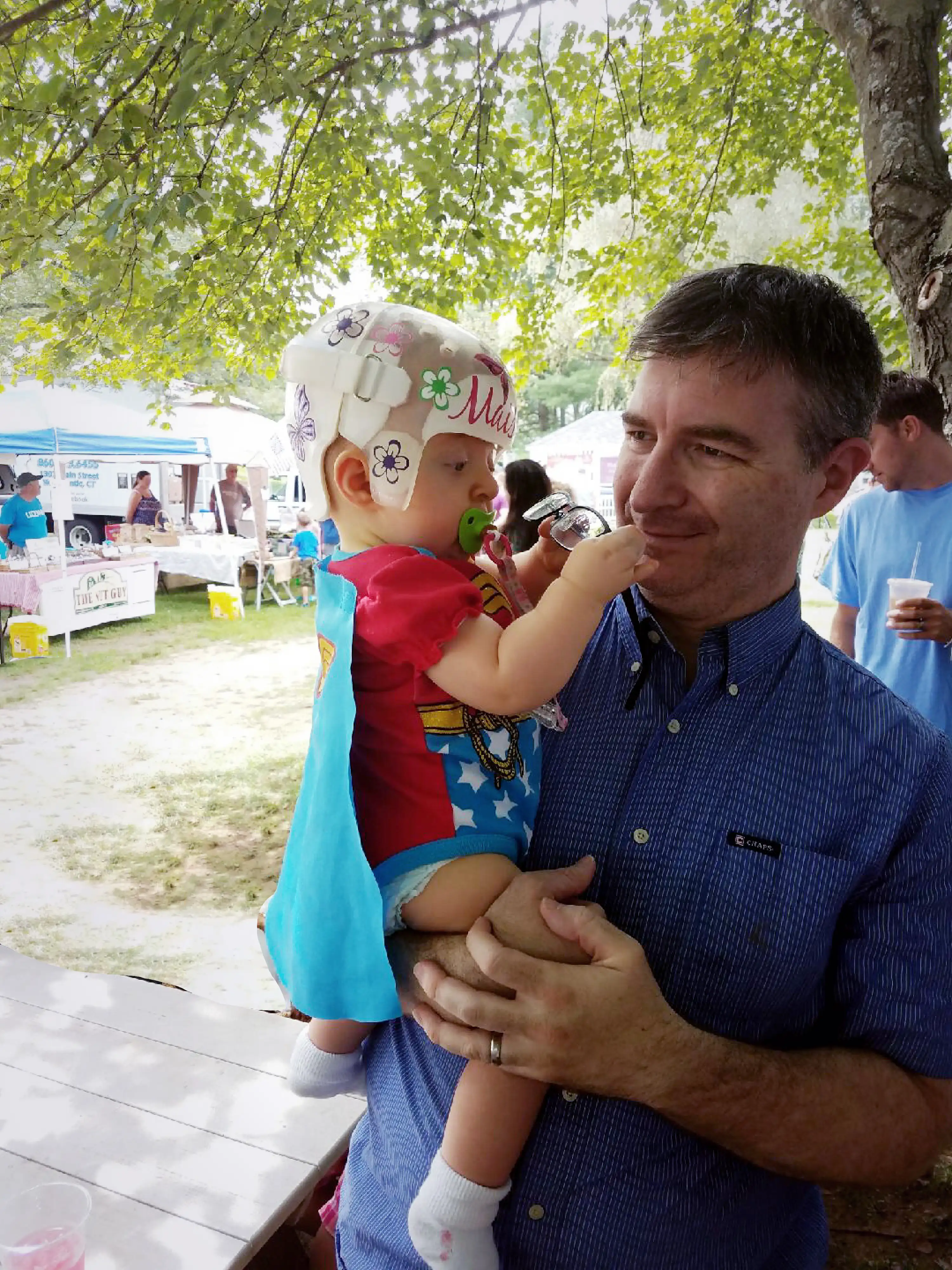 Older man holds up small child wearing costume with a cape