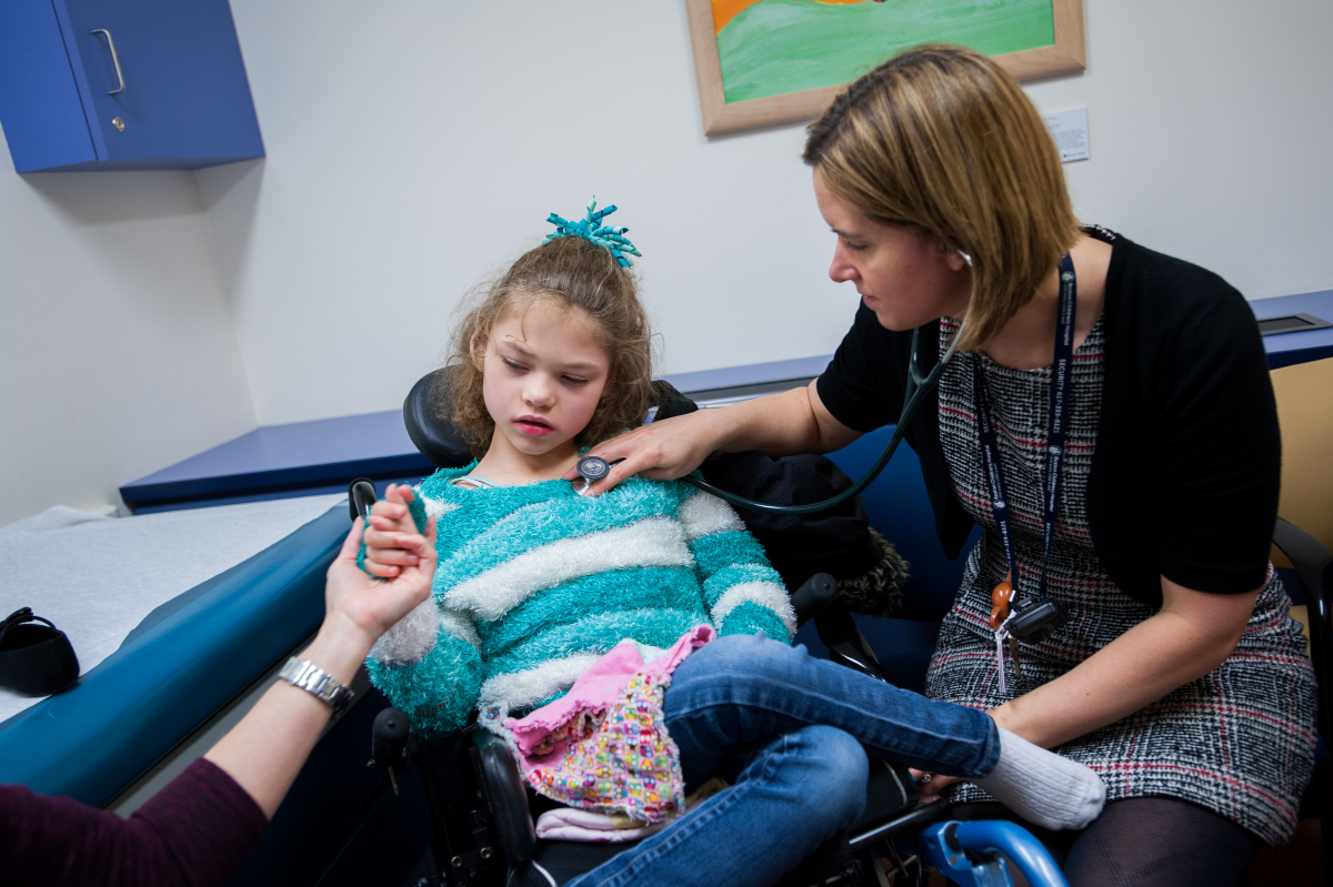 Clinician places stethoscope on sweater of young girl wearing sweater and jeans