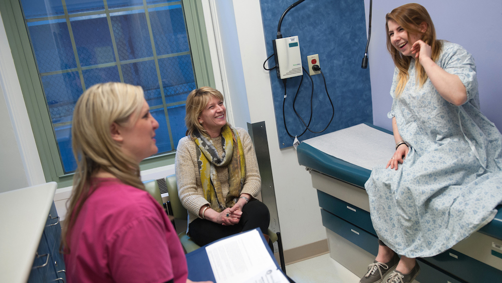 Doctor speaks with mother and teen patient wearing hospital gown