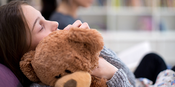 Young girl rests, holding teddy bear against herself