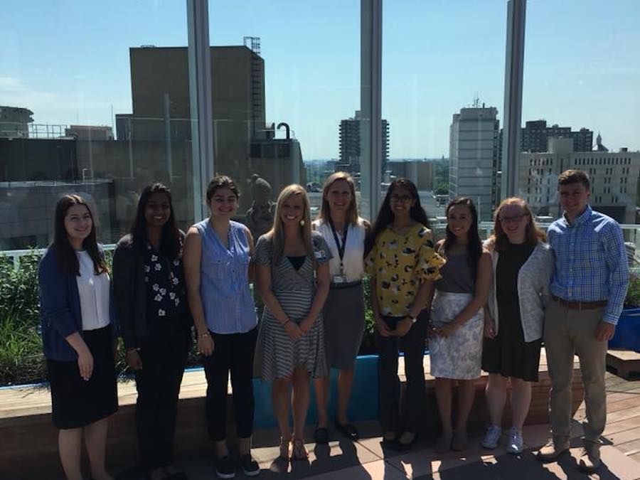 eight women and one man standing on outdoor roof deck overlooking city skyline