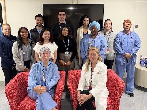 ten men and women standing and two women sitting in red chairs