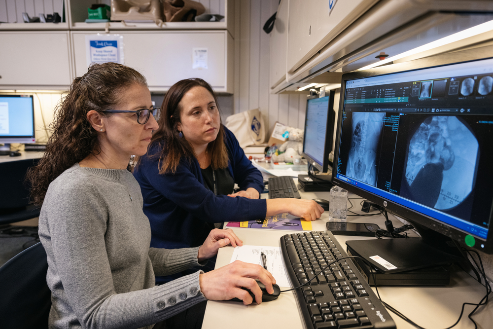 Two clinicians sit at table and look over imagery on computer monitor