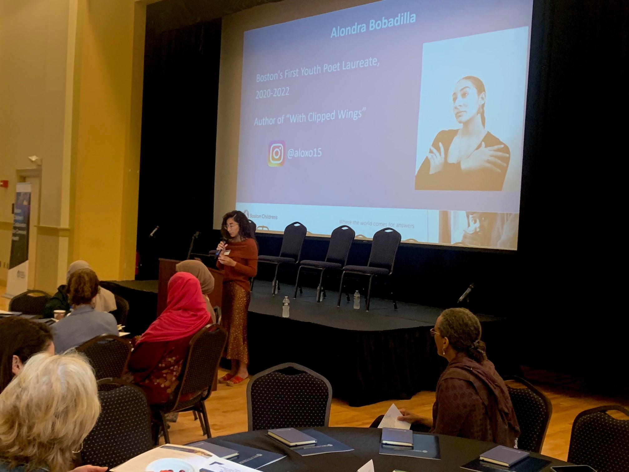 Woman in red dress is reading while she stands in front of a projector