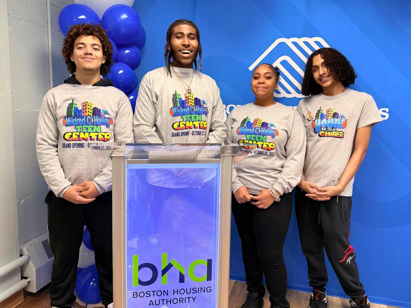Four teens wearing "Mildred C. Hailey Teen Center" shirts stand behind podium with Boston Housing Authority logo.