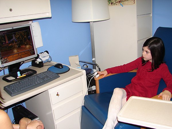 Girl sits on chair watching computer monitor propped up on desk