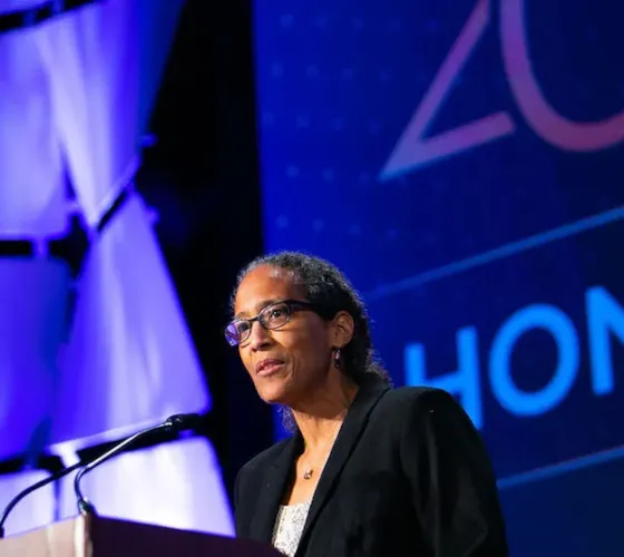 Woman with hair pulled back in ponytail and wearing glasses speaks at lecturn