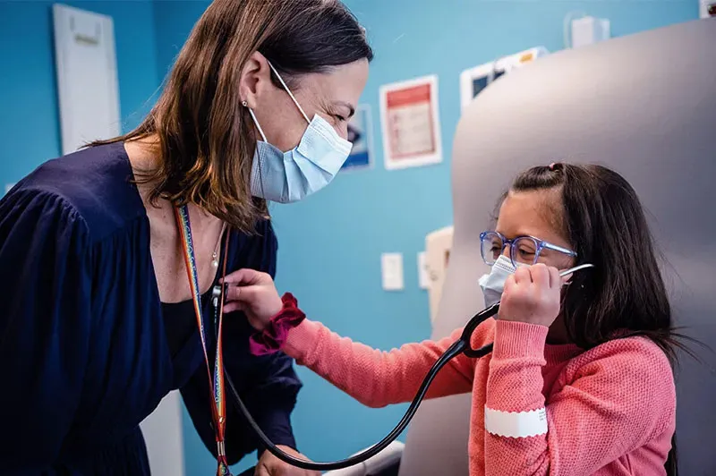 a girl holding a stethoscope to her doctors chest