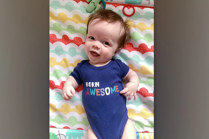 Toddler lay on blanket wearing onesie that reads: "Born Awesome"