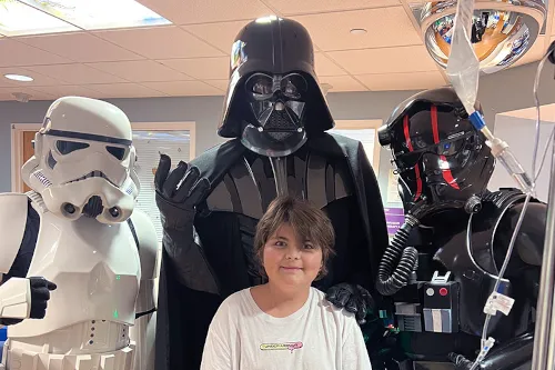 Young boy wearing T-shirt stands with three Star Wars characters behind him