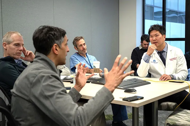 Man speaks and makes hand gestures while speaking with others in conference room