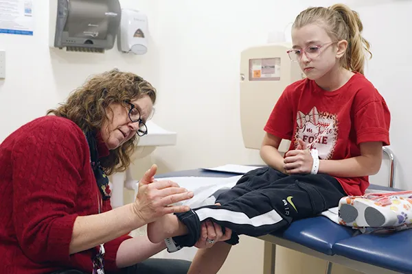 Female clinician, seated, closely examines a young girl's left ankle.