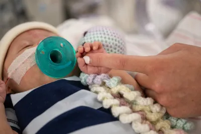 Adult's finger touches tiny hand of newborn in incubator