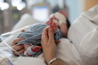 Adult touches tiny foot of newborn baby