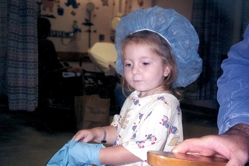 Girl wearing hospital scrubs and hair net looks downward, away from camera