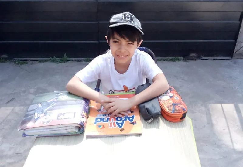 Agustín smiles while sitting at table with books in front of him