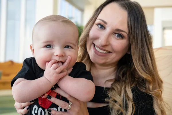 Toddler boy puts fingers in mouth, boy held tight by woman