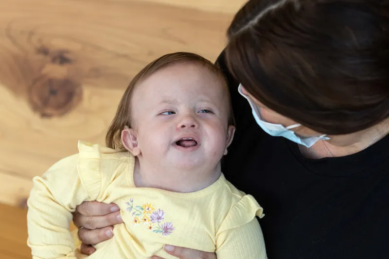 Girl in yellow shirt smiles as she's held by woman