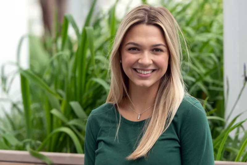 Young teen girl with blonde hair smiling in front of garden