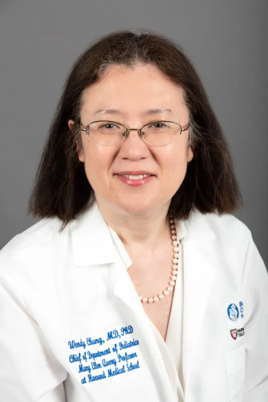 Woman wearing white doctor's coat and necklace and glasses, has shorter hair