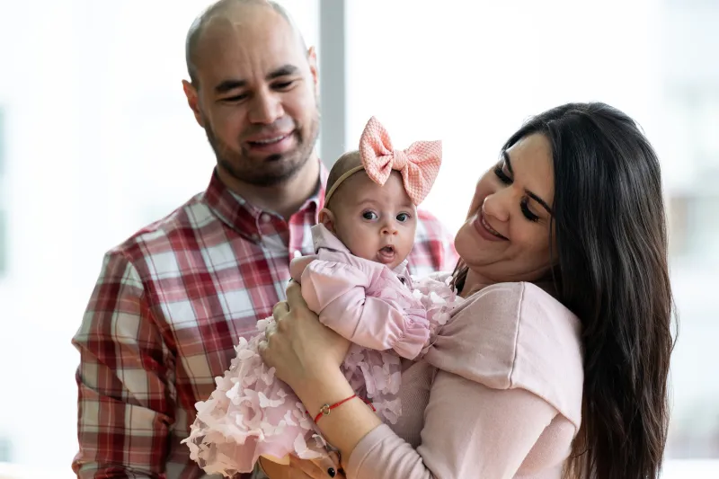 Woman gazes at child while holding child in arms. Man looks on lovingly from behind.