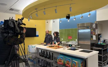 Camera crew films two adults standing behind kitchen island
