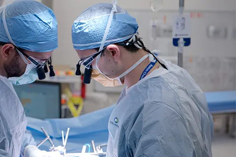 Two clinicians in scrubs and wearing glasses perform surgery