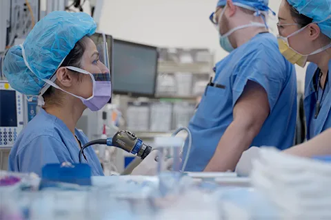 Clinician in scrubs looks away from camera, with two other clinicians in scrubs in background