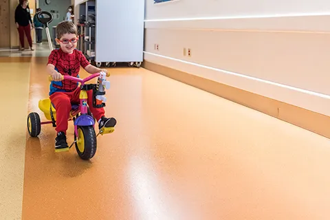 Boy rides small tricycle down unit hallway