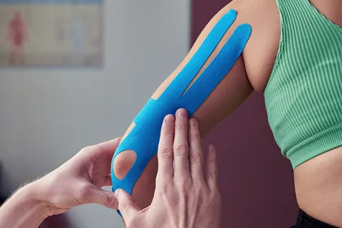 A person examines an athlete's taped-up left arm and elbow