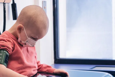 Toddler boy sits on exam table and looks at tablet
