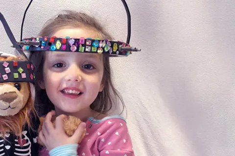 Girl wearing halo brace holds teddy bear who's also wearing halo brace