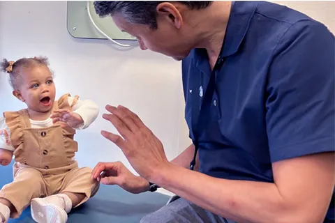 Clinician on right pats hands with young girl sitting on exam room table